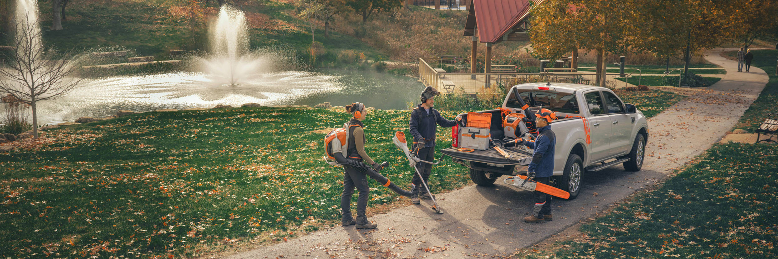  Eine Gruppe professioneller Landschaftsgärtner steht um ihre Fahrzeuge herum und bereitet sich mit STIHL Akku-Geräten auf ihre Arbeit vor.