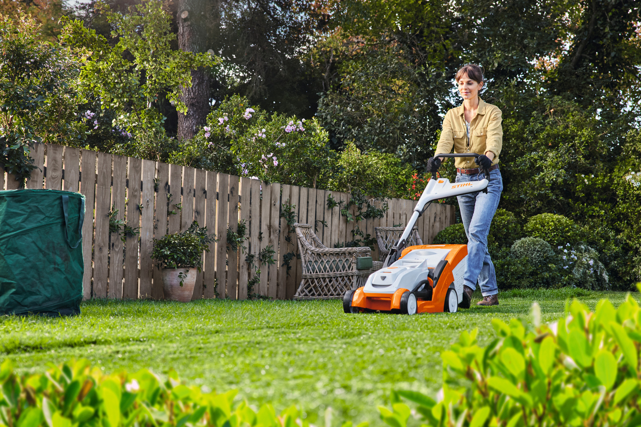 Mann betreibt mit STIHL Rasenmäher RMA 448 TC auf einem bewachsenen Grundstück Rasenpflege im Sommer