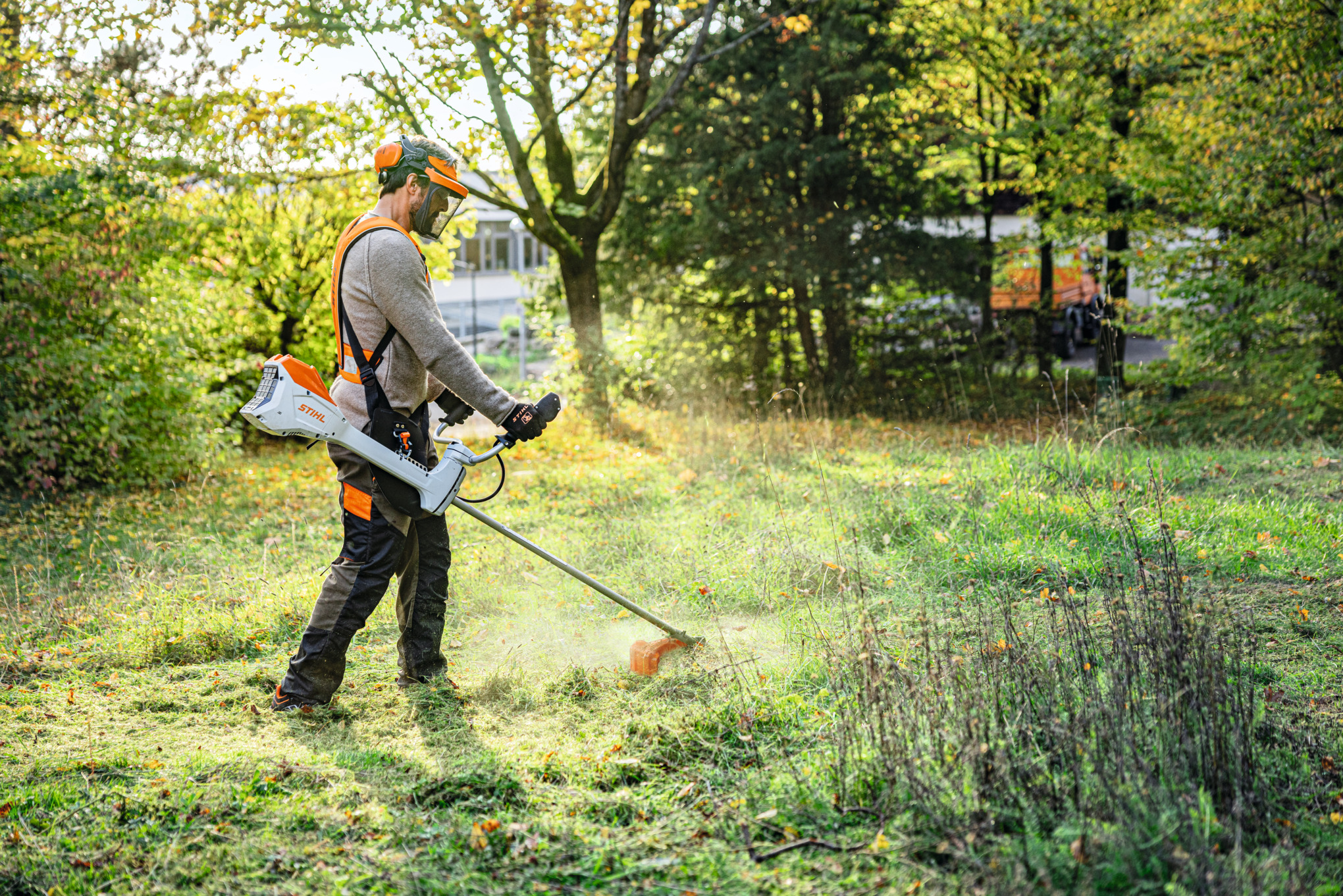 Ein Mann mäht mit dem Akku-Freischneider STIHL FSA 200 eine Grünfläche in einem Park 