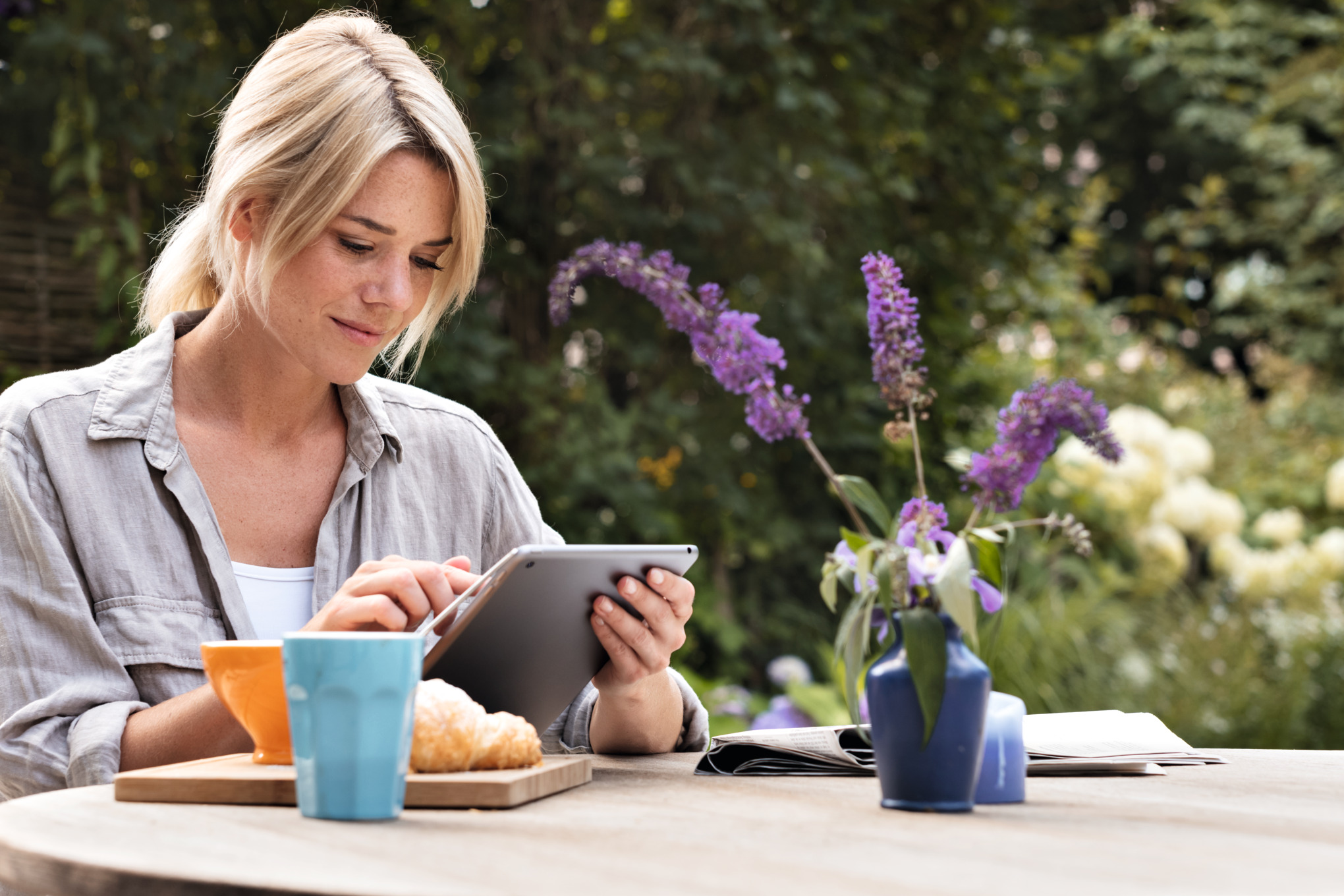 Frau benutzt ein Tablet am Frühstückstisch im Garten