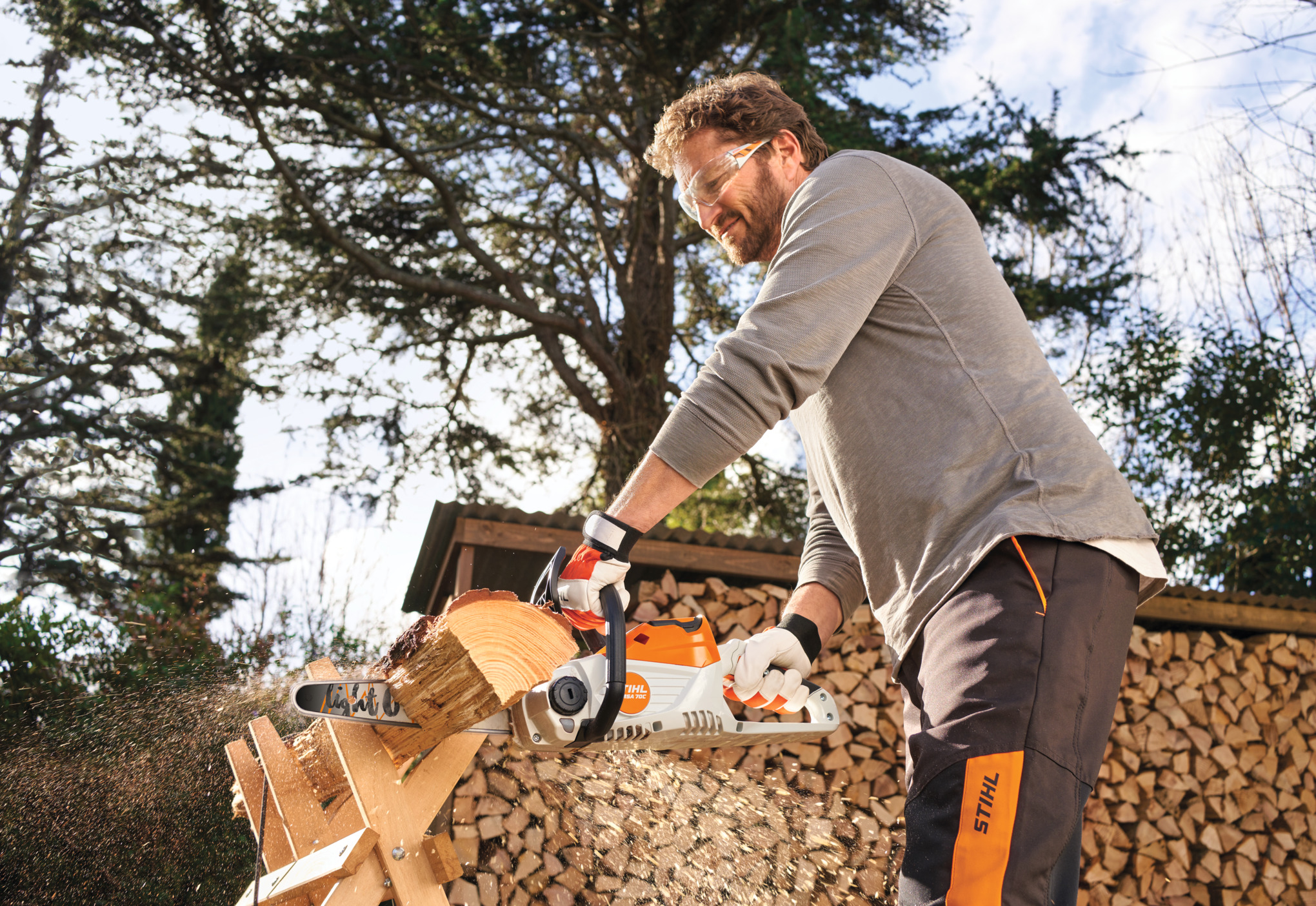 Ein Mann sägt mit einer STIHL Motorsäge Holz auf einem Sägebock