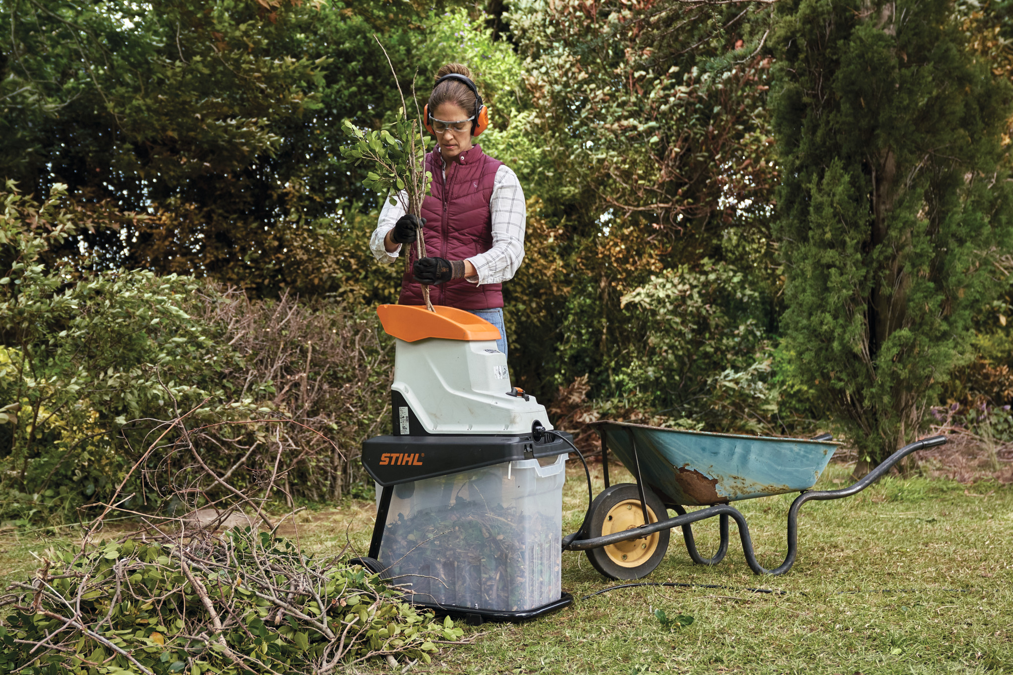 Eine Frau in Schutzausrüstung zerkleinert einen Ast mit einem Elektro-Gartenhäcksler STIHL GHE 140 L