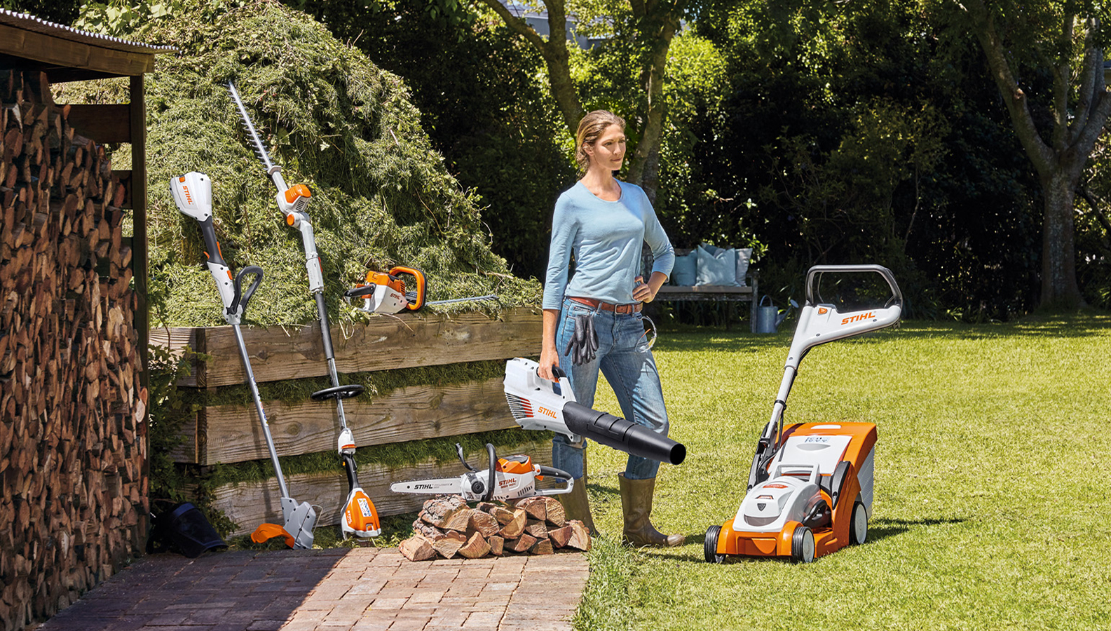 Frau steht im Garten mit einer Auswahl an Akku-Produkten von STIHL