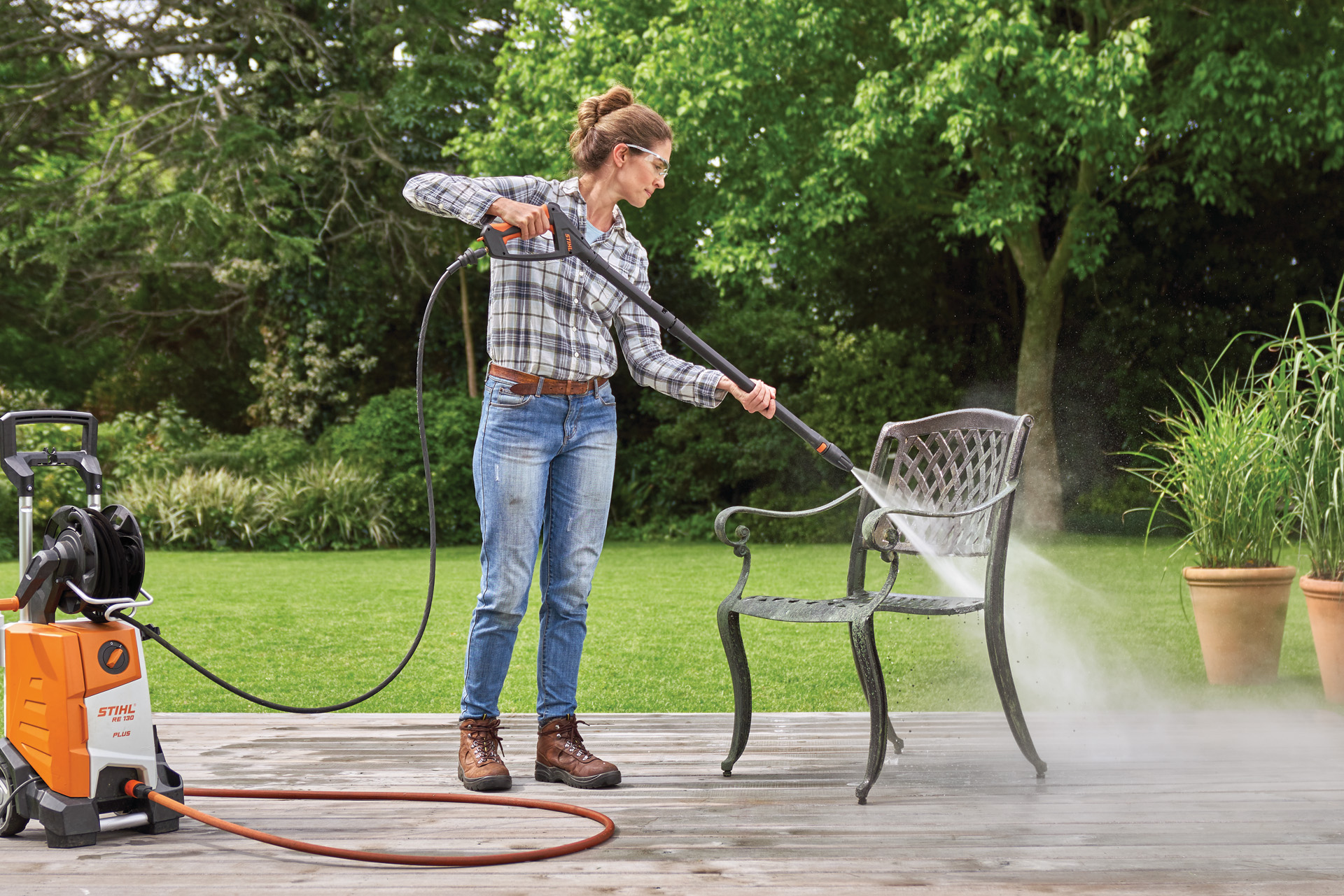 Frau reinigt Gartenstuhl aus Metall auf der Terrasse mit dem STIHL Hochdruckreiniger RE 130 plus