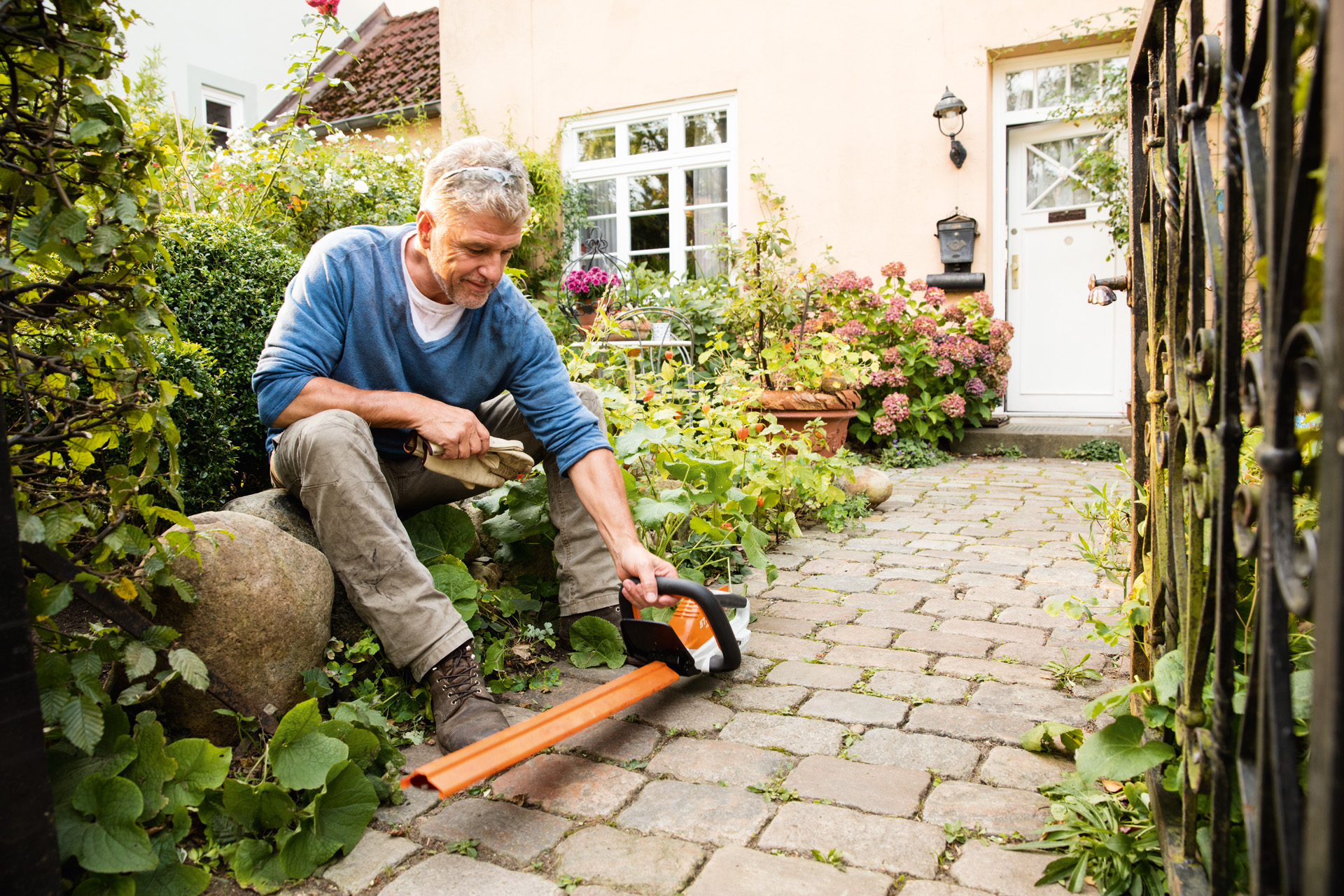 Mann mit STIHL Elektro-Heckenschere HSA 45 der AI-Linie vor einem Haus