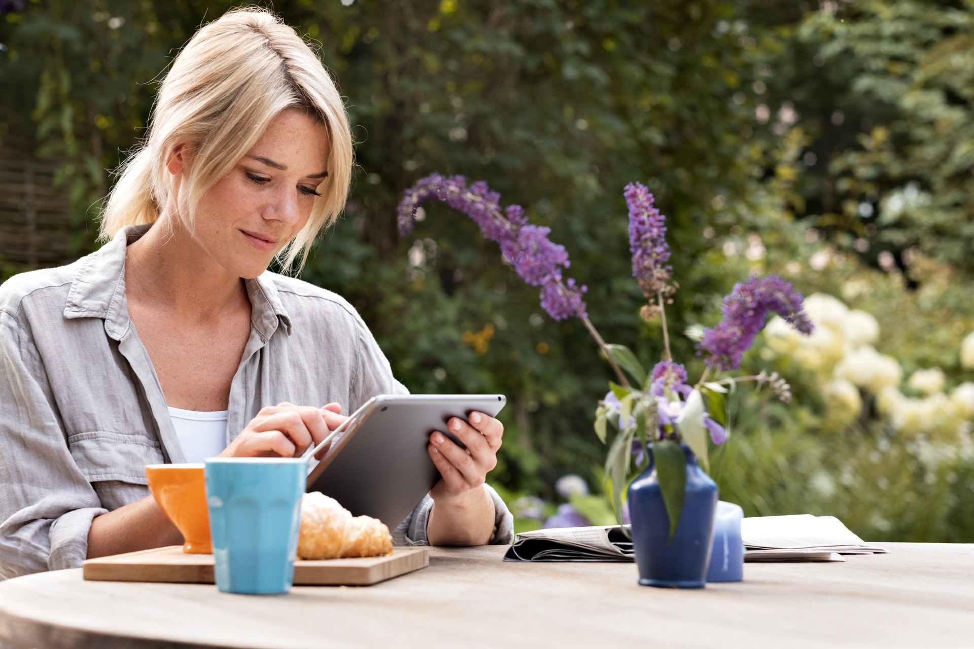 Frau bedient Tablet am Frühstückstisch im Garten