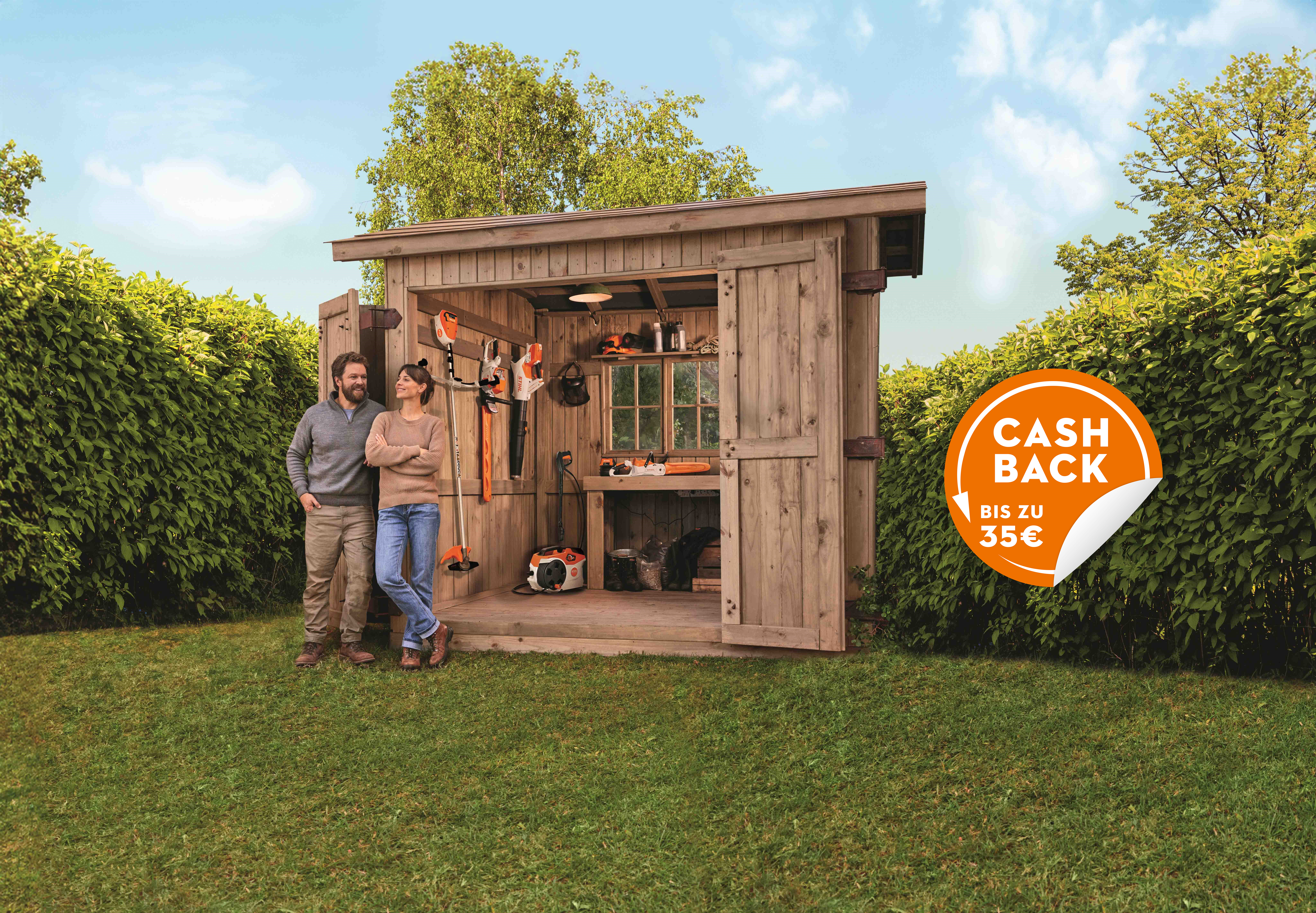 Diverse STIHL Akku Produkte aus dem Akku AK-System auf einem Rasen mit zwei Personen vor einer Holzhütte und Cashback Badge.