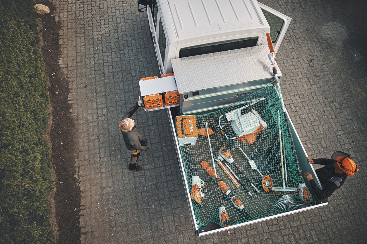 Zwei STIHL Profis in Vogelperspektive an einem Fahrzeug, beladen mit bottTainer und STIHL Akkugeräten.